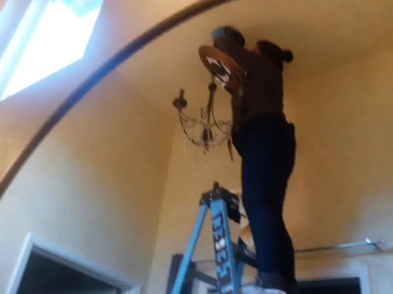 Electrician installing a chandelier in a Orosi residence